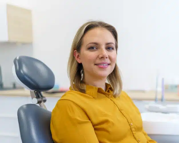 Smiling woman in a yellow blouse seated comfortably in a dental chair