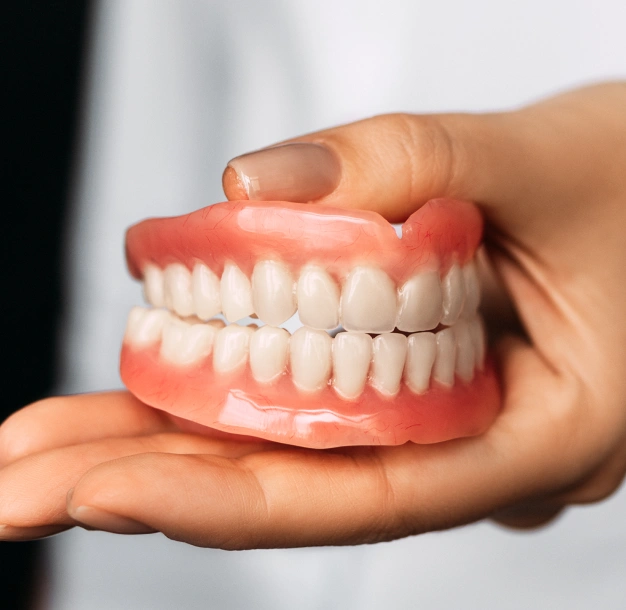 Hand holding a complete set of upper and lower dentures with pink gums and white teeth