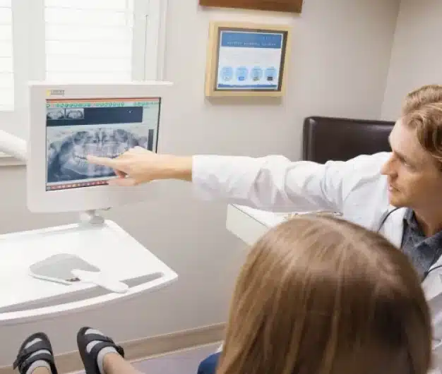 Dentist pointing to a dental X ray on a monitor while reviewing the results with a young patient