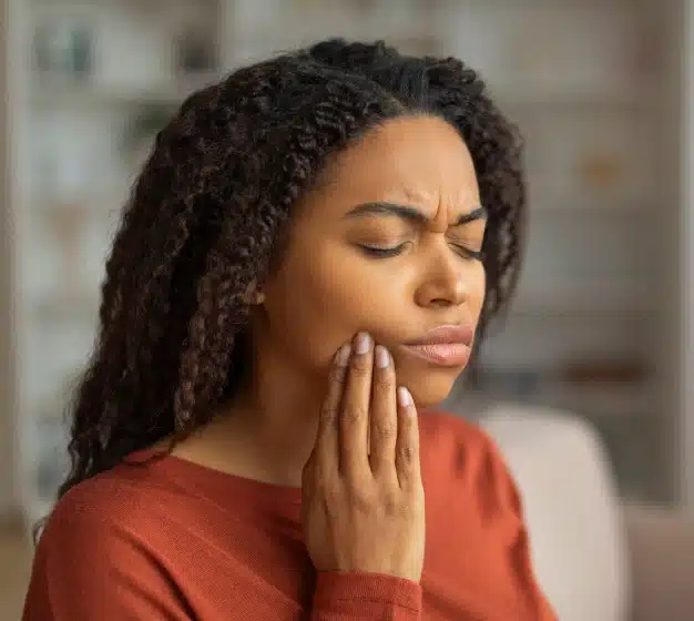 Woman holding her cheek and grimacing from tooth pain, indicating a dental emergency