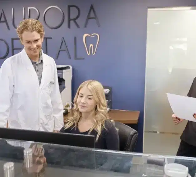 Aurora Dental dentist and front desk staff reviewing patient information at the reception computer