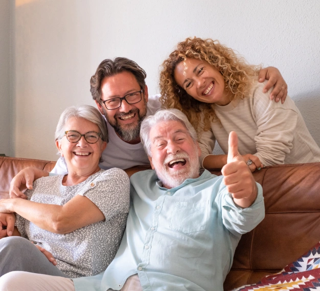 Multigenerational family laughing together on a couch with one member giving a thumbs up