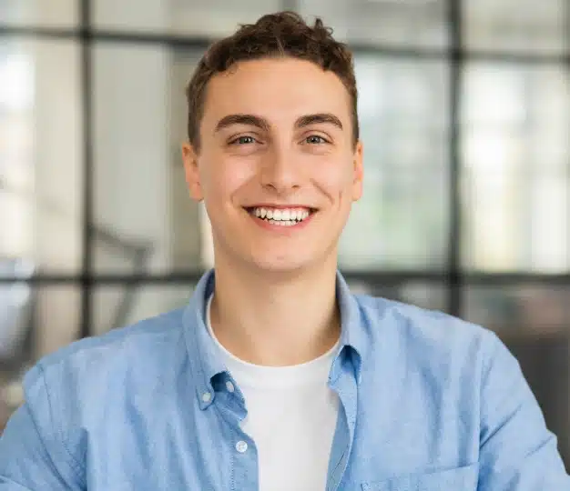 Smiling young man in a light blue button down shirt showing a bright, healthy smile