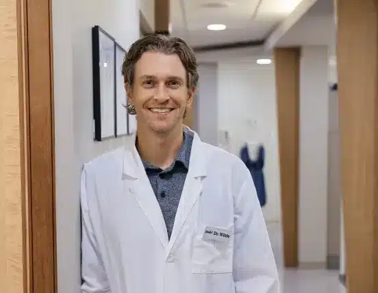 Dr. Wilde smiling in a white coat standing in the hallway of the Aurora Dental office