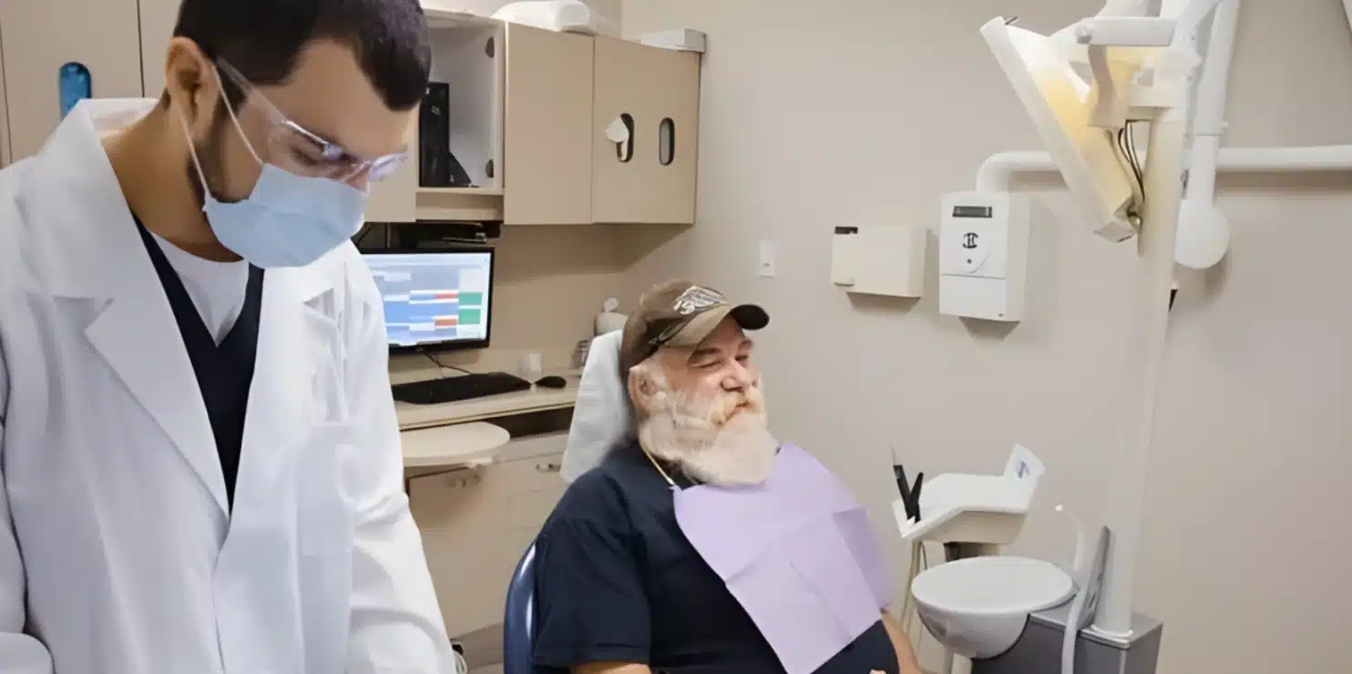 A dentist in a white coat consulting with an elderly male patient in the dental chair
