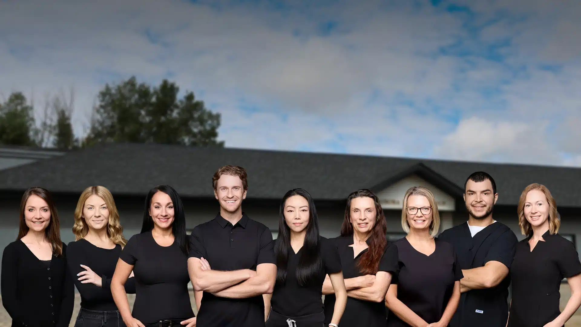 The Aurora Dental Group team posing together in black uniforms outside the dental office in Lacombe AB
