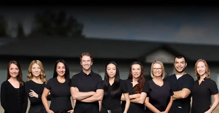 The Aurora Dental Group team posing together in black uniforms outside the dental office in Lacombe AB