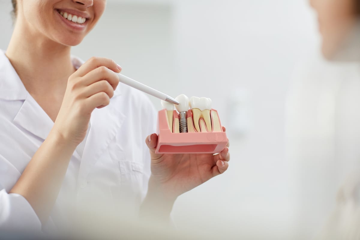 Dentist demonstrating dental implant model with crown and implant components to patient.