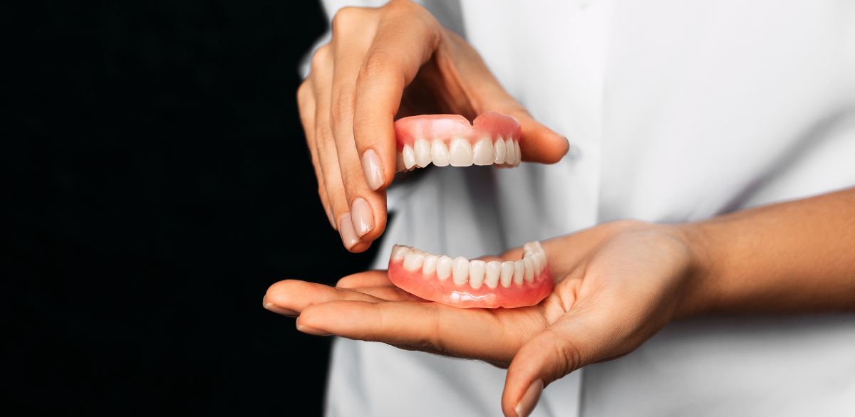 Hands holding full dentures for tooth replacement options.