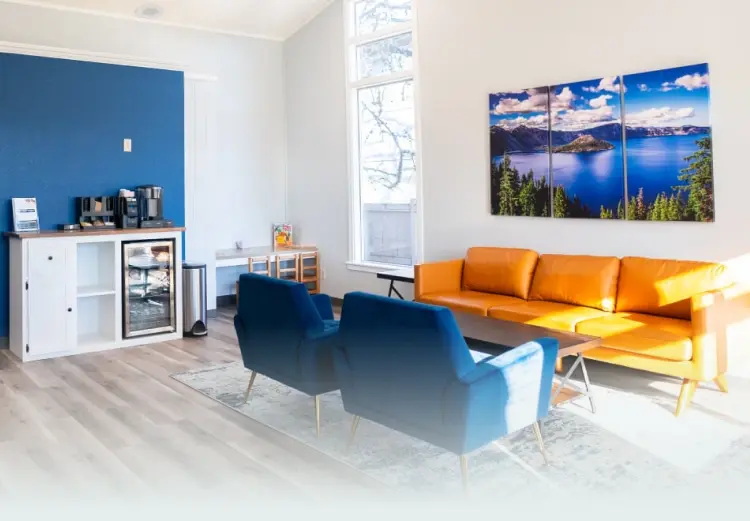 Modern dental office waiting room with blue accent wall, orange sofa, and large window in Grants Pass.
