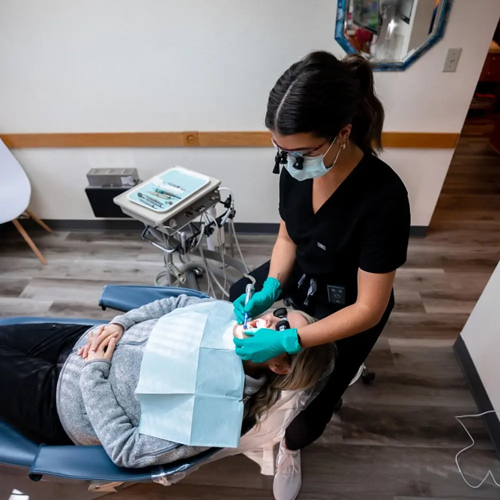 Dental hygienist performing oral examination on patient in treatment room.