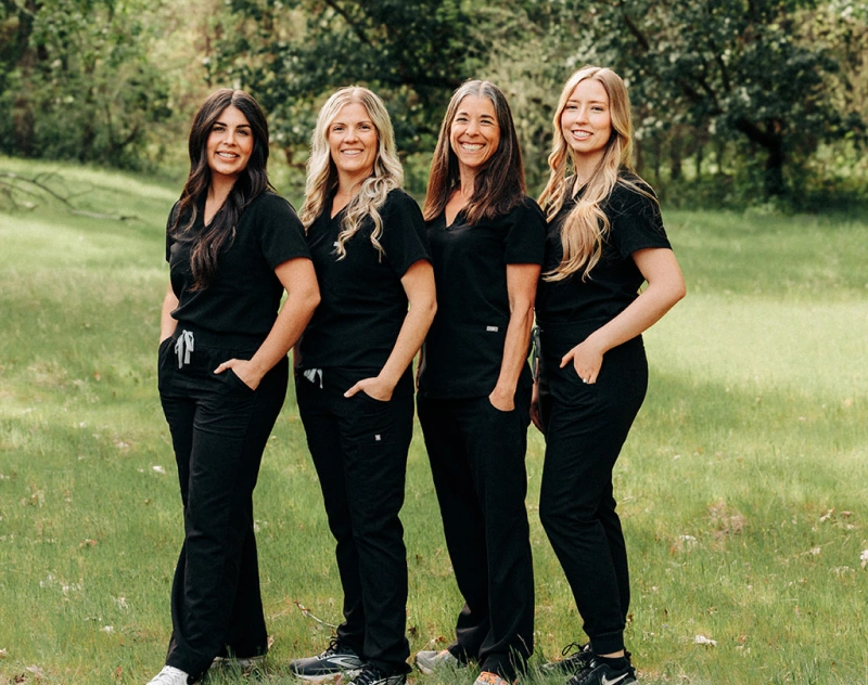 Four smiling women in black uniforms standing outdoors in Grants Pass, Oregon.