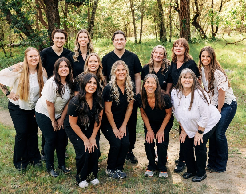 Dental practice team of 13 smiling professionals posing together outdoors in Grants Pass, Oregon.
