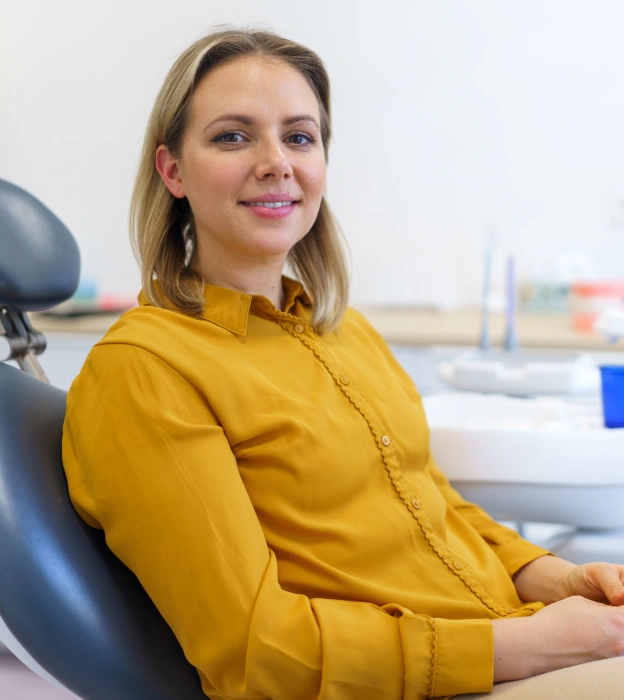 Woman in yellow shirt smiling in a dental office treatment room.