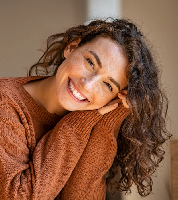 Woman smiling brightly while wearing a rust-colored sweater, showcasing a healthy, radiant smile.
