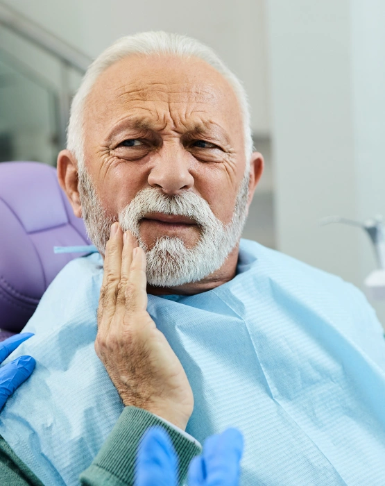 Older male patient experiencing tooth pain, holding his cheek during dental consultation in Grants Pass.