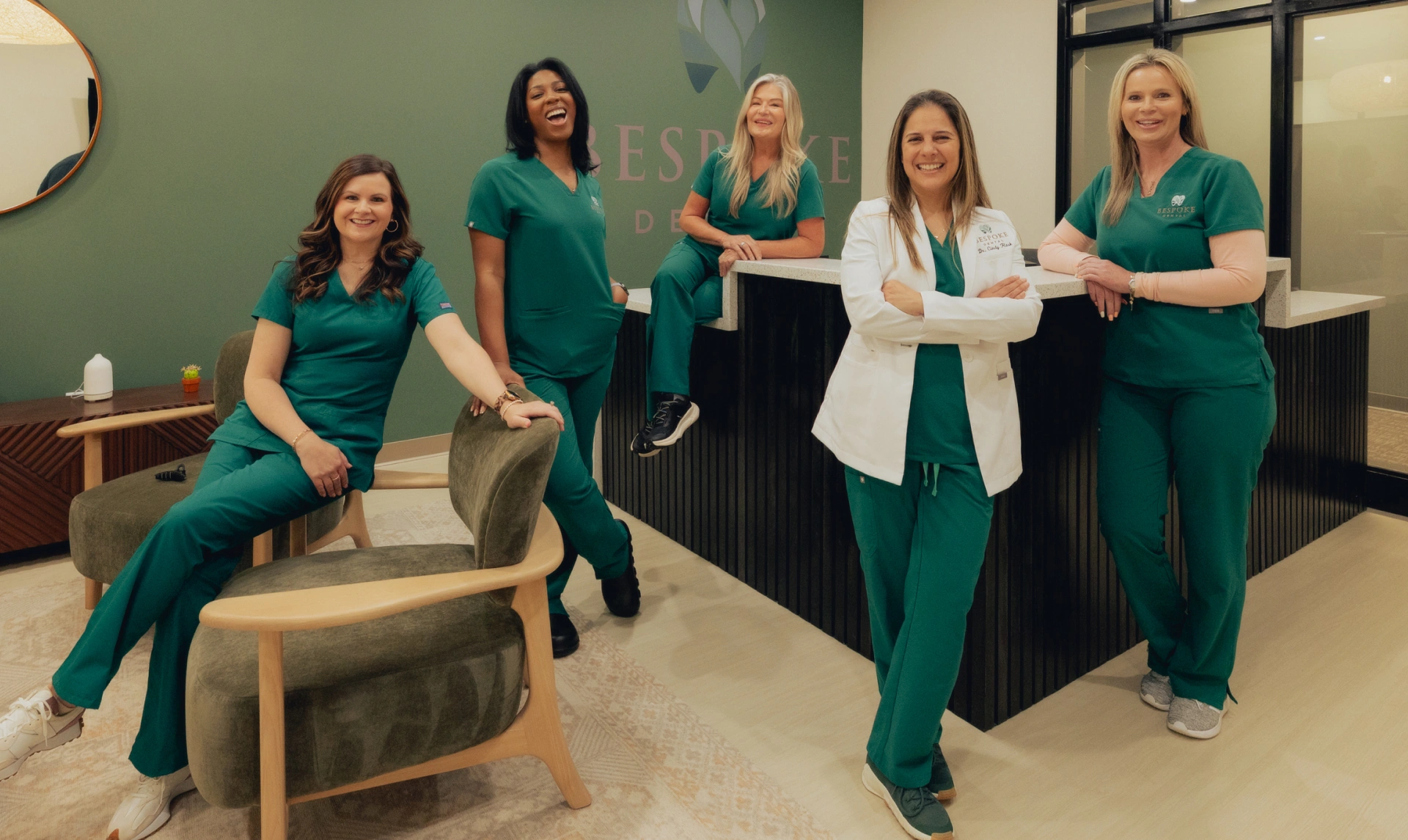 Five dental professionals in green scrubs posing together in a modern dental office in Newnan, GA.