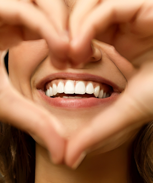 Happy patient with bright white teeth framed by hands making a heart shape.