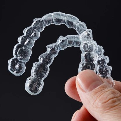 Clear aligners held in hand showing Invisalign treatment trays for straightening teeth.