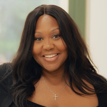 Smiling woman with long dark hair wearing a cross necklace and black top.
