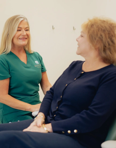 Dental hygienist in green scrubs shaking hands with patient during prophylaxis consultation.