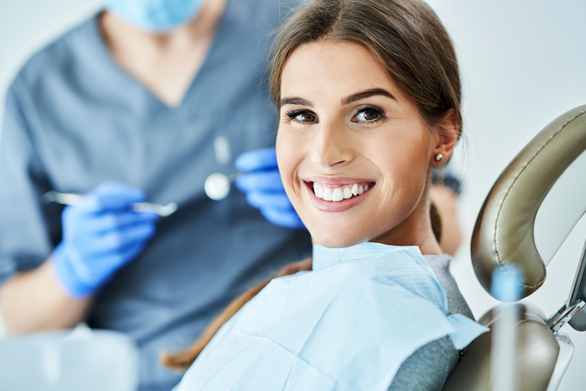 Smiling dental patient in treatment chair with dentist in blue gloves during examination.