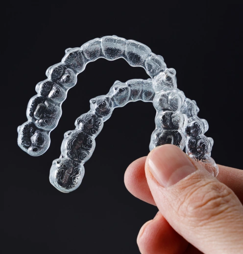 Clear dental aligners held in hand showing transparent orthodontic treatment trays.