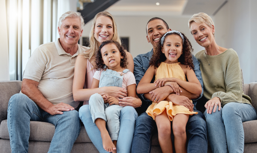 Multi-generational Newnan family smiling together on couch for dental practice.
