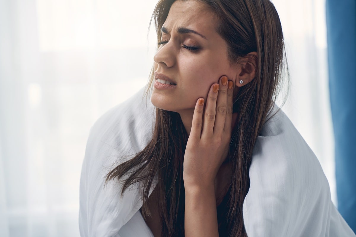 Woman holding cheek due to severe throbbing tooth nerve pain