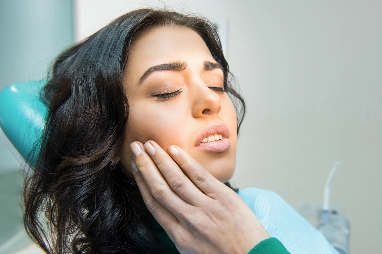 Woman with TMJ pain holding her jaw while seated in dental chair.