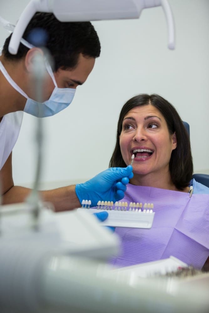 Dentist showing tooth shade samples to smiling patient during holistic dental consultation.