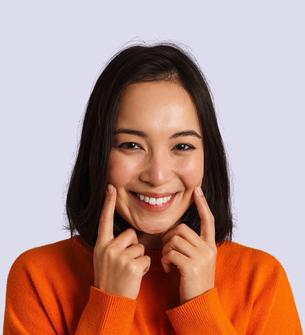 Smiling woman in orange sweater touching her face, representing improved comfort from TMJ and orofacial pain treatment.