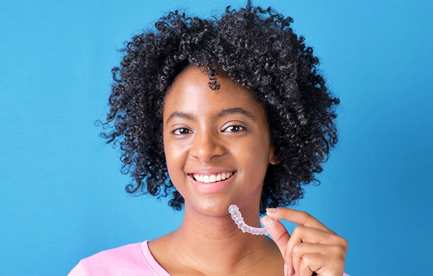 Young woman smiling while holding an invisible aligner for orthodontic treatment.