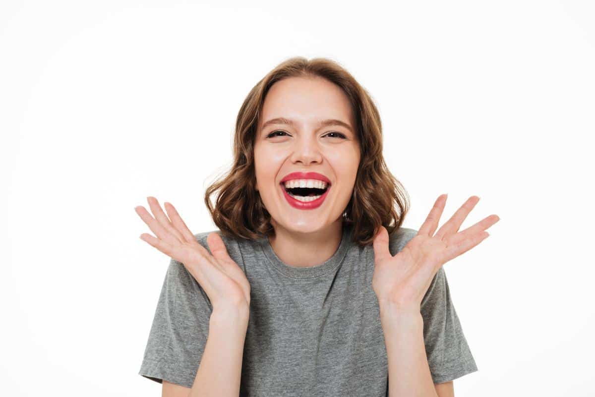 Woman in gray shirt smiling with hands raised in excitement against white background