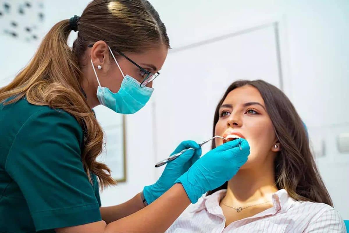 Dental hygienist examining patient's teeth in modern clinic with protective mask and gloves.