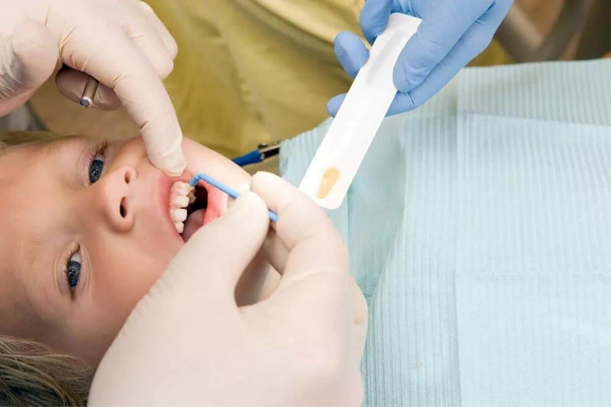 Child receiving dental examination with gloved dentist hands holding tools in dental office setting.
