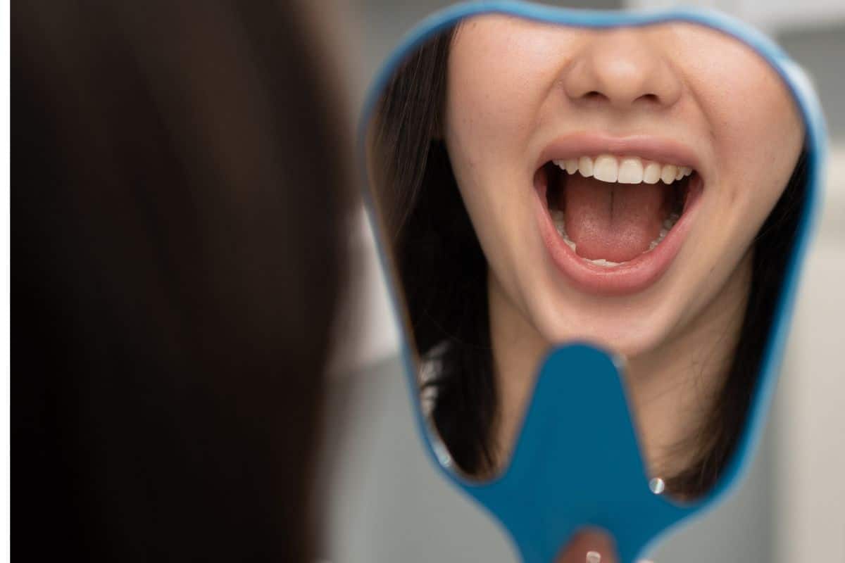 Woman examining her gum health in a mirror to see if she may qualify for dental implants dental implants sandy