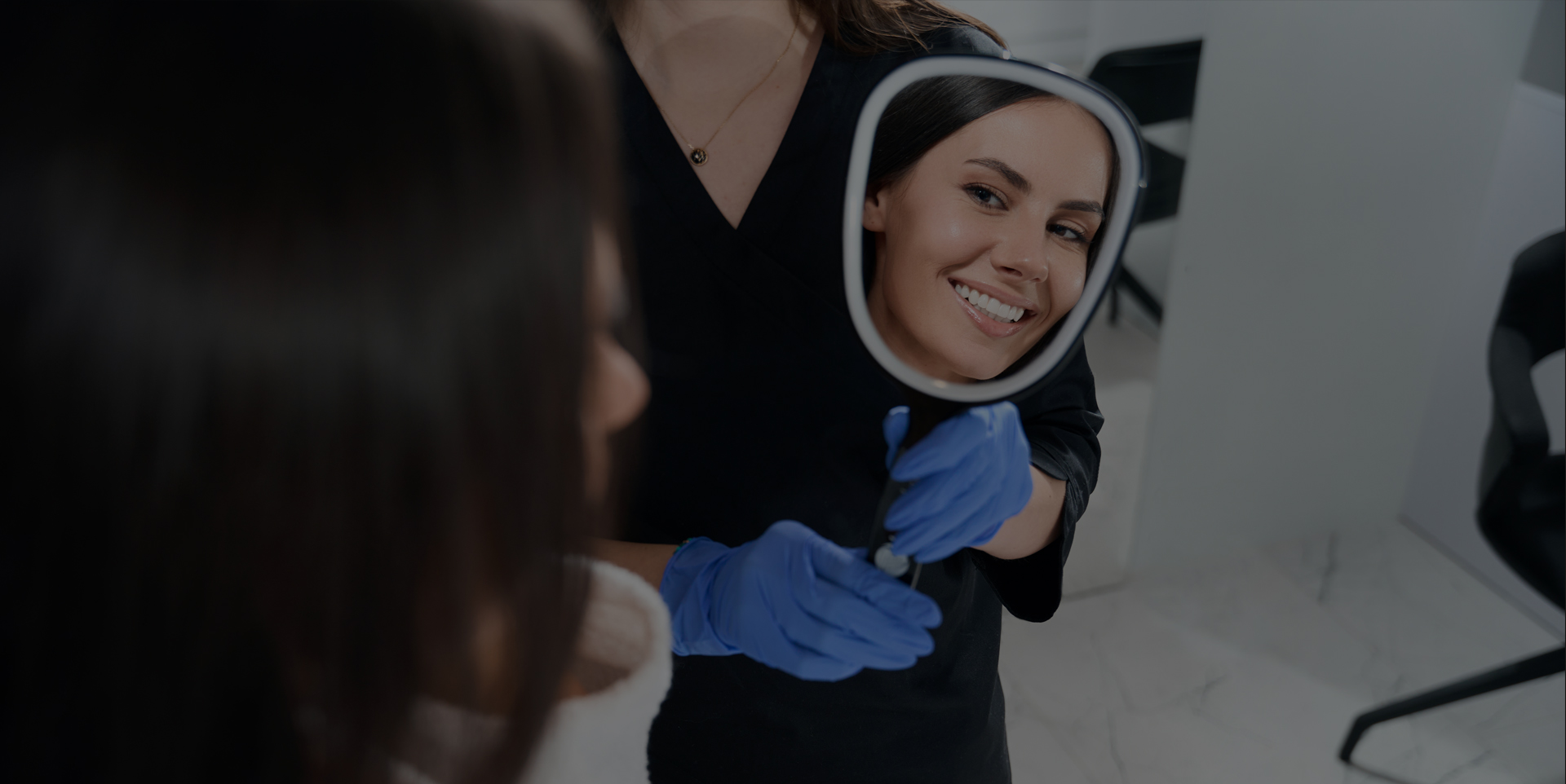 Dental assistant holding a mirror while a woman checks her teeth after an exam and cleaning at Coastal Dental Arts in Peabody, MA