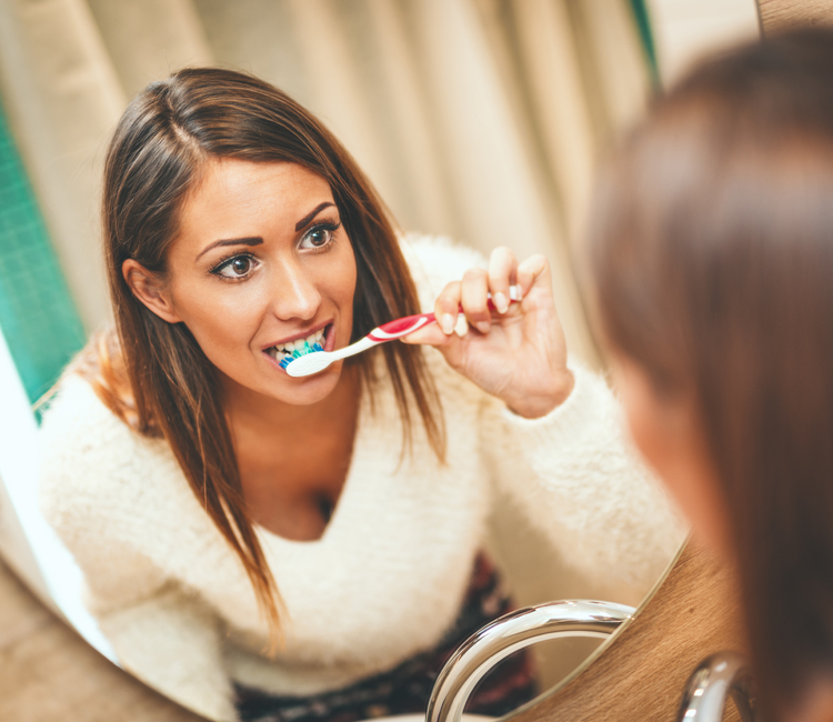 dental exams and cleanings peabody. Young woman brushing her teeth with a toothbrush at Coastal Dental Arts in Peabody, MA