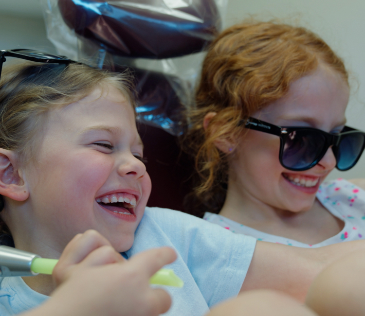Two children wearing sunglasses smiling after a routine pediatric dental care visit at Coastal Dental Arts in Peabody, MA