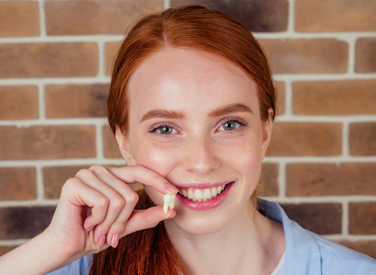Tooth extraction Peabody. Woman smiling while holding a damaged, extracted tooth at Coastal Dental Arts in Peabody, MA
