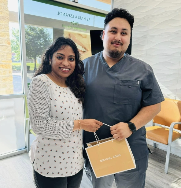 Two people smiling at a dental office, one holding a Michael Kors shopping bag.