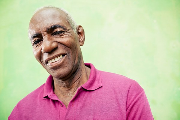 Older man in a pink shirt smiling warmly at the camera