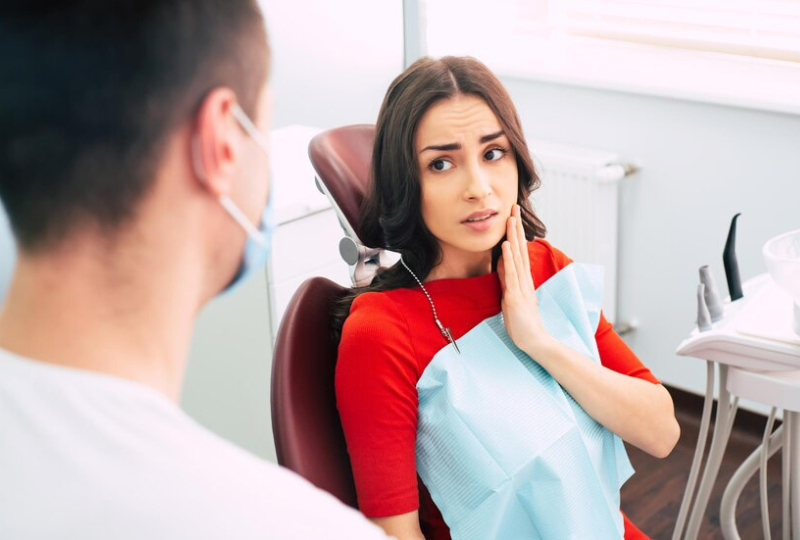 Dentist speaking with a female patient who is holding her jaw in pain