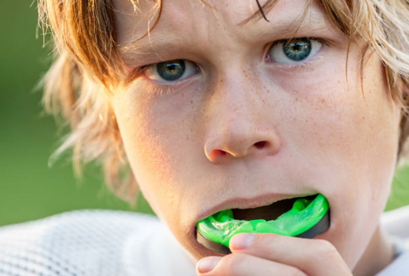 Young boy wearing a green athletic mouthguard outdoors
