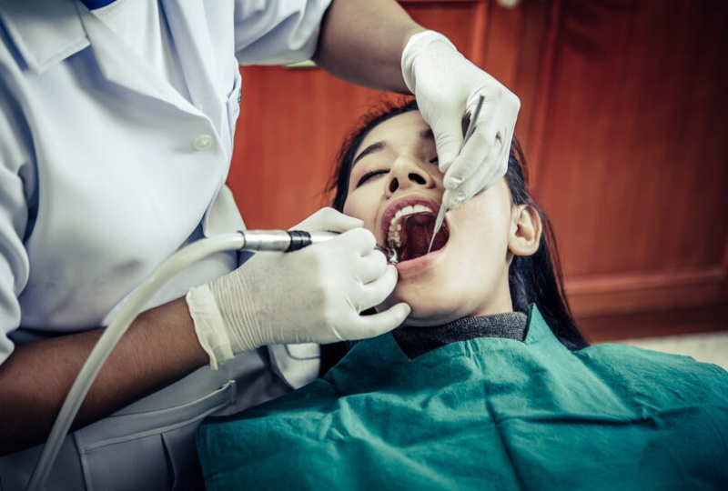 Dentista con mascarilla examinando a un paciente en el sillón dental en una clínica.