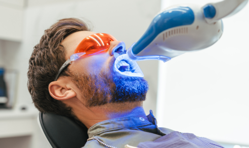 Dentist using a blue UV curing light on a male patient during a procedure