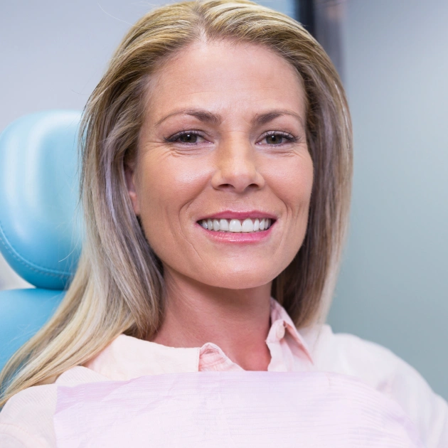 Smiling middle aged woman sitting in a dental chair wearing a dental bib during a checkup