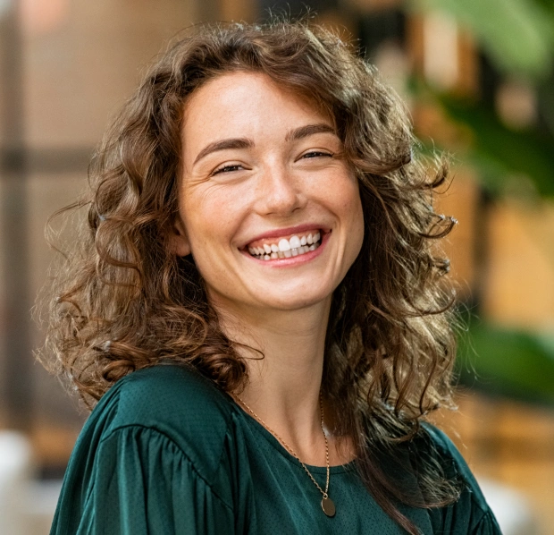 Portrait of a young woman with curly hair smiling in a bright outdoor setting