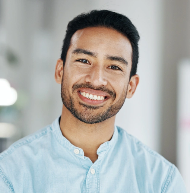 Portrait of a smiling young man in a light blue shirt against a soft background